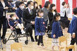 紅白幕が掛けられた会場に入場してくるベビーカーに乗っている園児と卒園児たちの写真