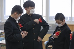 胸にさした赤い花を見せあっている男子卒業生3人の写真