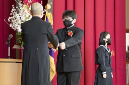 校長先生から卒業証書を受け取っている黒いマスクをした卒業生の写真