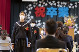 祝卒業と書かれた看板を背に体育館を退場している卒業生の写真