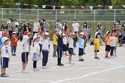 白い帽子をかぶっている園児たちがグラウンドで準備運動をしている様子の写真