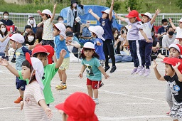 紅白帽をかぶった園児たちがグラウンドで準備運動をしている様子の写真