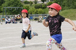 赤い帽子をかぶった女児2人がグラウンドを走っている写真