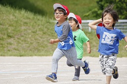 赤い帽子をかぶった男児3人がグラウンドを走っている写真