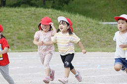 赤い帽子をかぶった女児2人が手をつないでグラウンドを走っている写真