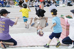 障害物レースでお面を付けて逆上がりをしている園児の写真