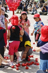 赤い帽子をかぶった園児たちがグラウンドで玉入れをしている様子の写真