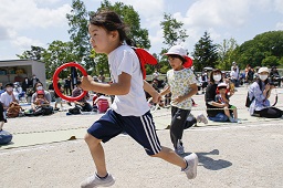 それぞれ赤い輪っかと白い輪っかを持った女児2人がグラウンドで競争をしている写真