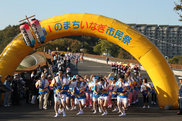 Iのまち いなぎ市民祭と書かれた黄色いアーチの下を踊っている市民のみなさんの写真