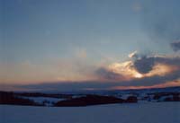 一面の雪原に夕日が沈んでゆく様子の写真