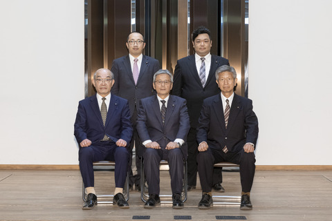 紺色のスーツ姿の男性を真ん中に、前3名が座り後ろ2名が立ち正面を向いている写真