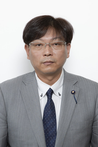 ライトグレーのスーツに紺色の水玉のネクタイをしめてめがねをかけている川村淳さんが正面を向いている写真