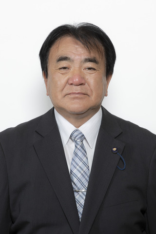 黒いスーツに薄いブルーのチェックのネクタイをしめた齋藤宏司さんが正面を向いている写真