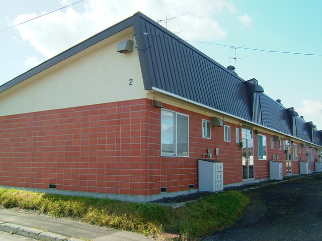 青空を背景にレンガ調の壁とへの字型の屋根が特徴の長屋住宅の写真