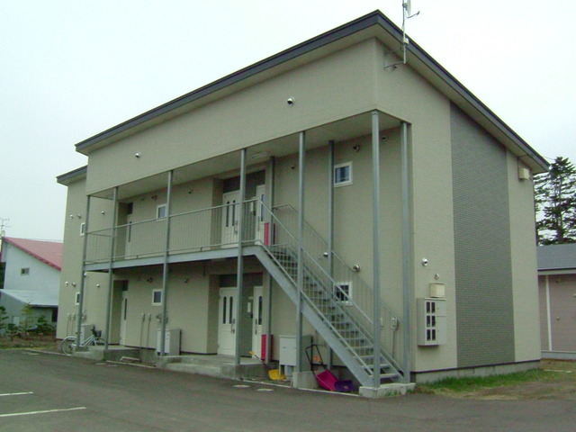 目の前にアスファルトの駐車場がある片流れ屋根の2階建ての共同住宅の写真