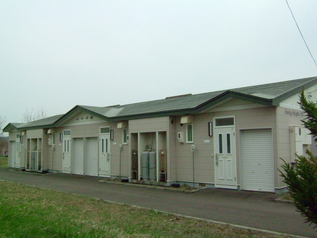 曇り空を背景に白いドアと緑色の屋根の長屋住宅の写真