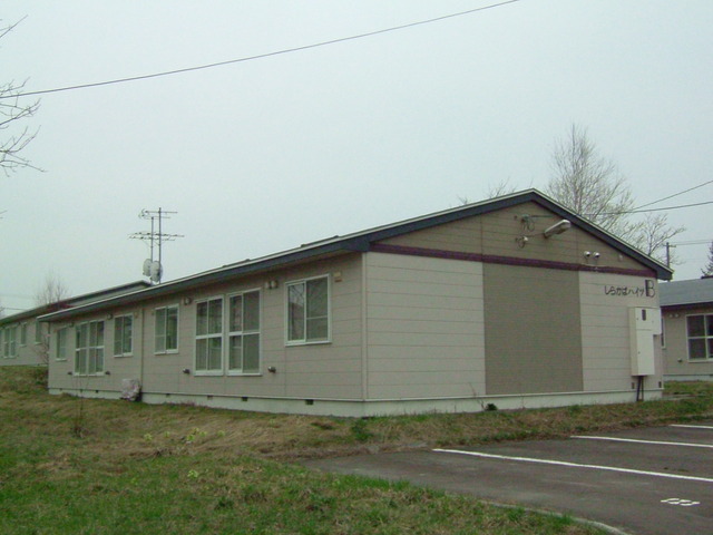 曇り空を背景に目の前に芝生とアスファルトの駐車場がある長屋住宅の写真