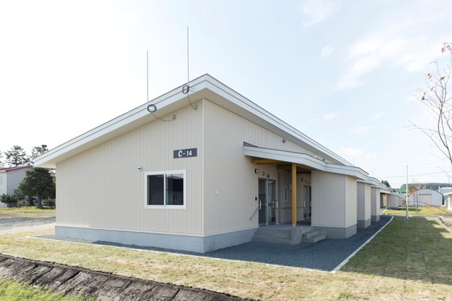 青空を背景に芝生に囲まれた白い壁で片流れ屋根の長屋住宅の写真