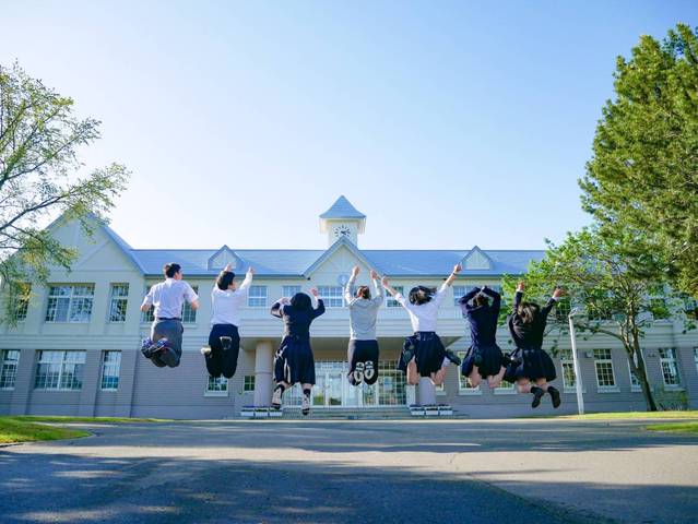 高校の校舎の前で7人の生徒がジャンプしている写真