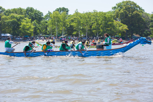 青い龍に模られた長いボートを緑色のライフジャケットを身に着けた数名の男達が必死で漕いでいる様子の写真