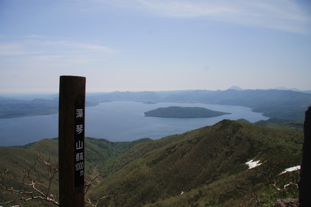 眼下に広がる山並みと湖をバックに藻琴山の山頂標識を写した写真