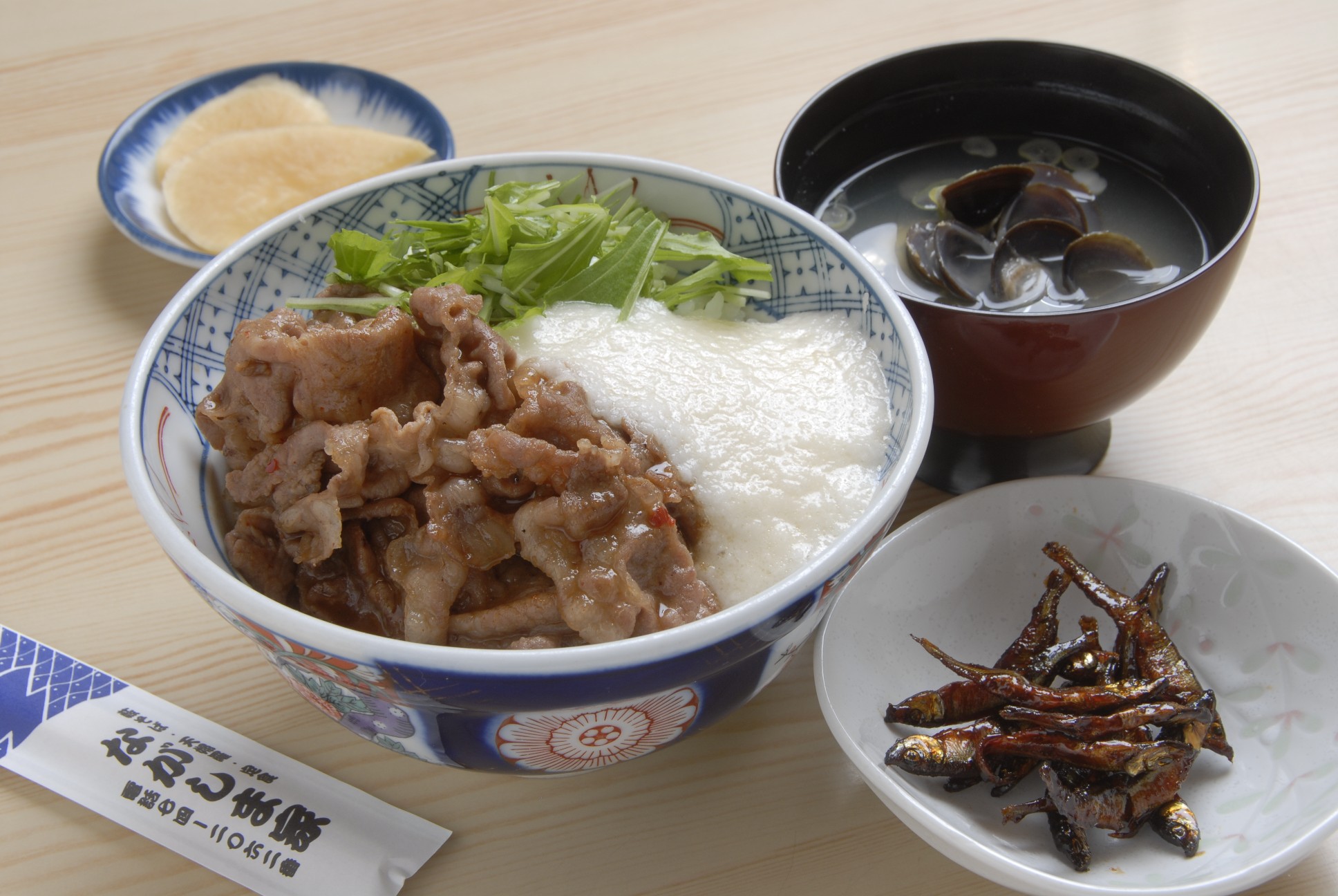 ごはんの上に豚肉を焼いたもの、とろろ、水菜がのったどんぶり、お吸い物、小魚と漬け物の2つの小皿がついた定食の写真