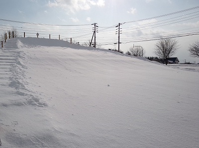 丘の斜面が雪で覆われ大きなすべり台のようになっている写真