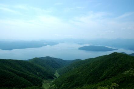 藻琴山山頂から望む、緑の山々に囲まれ豊富に水を湛えた屈斜路湖の遠景の写真