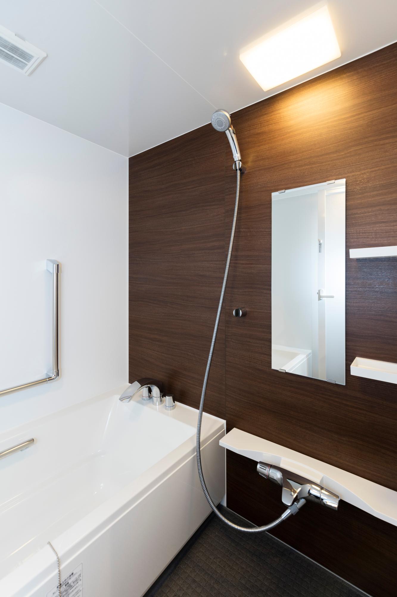 木目調パネルの濃茶色の壁と、清潔感のある白いバスタブが設置されている浴室内の写真